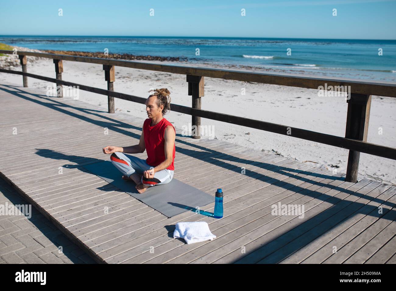 Mann meditiert während er an sonnigen Tagen am Strand Yoga auf dem Boden praktiziert Stockfoto