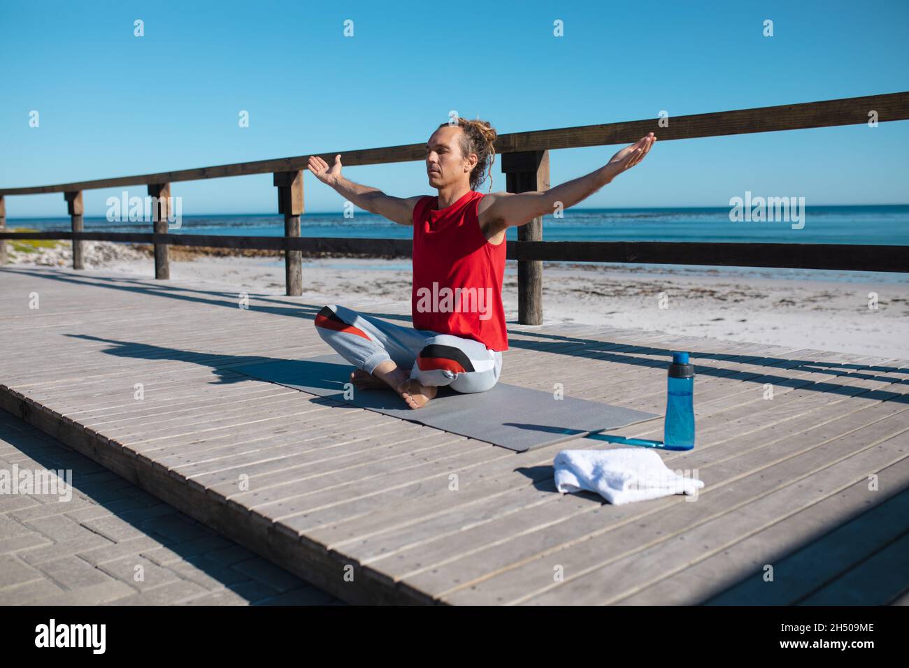 Mann, der mit gekreuzten Beinen und ausgestreckten Armen sitzt, meditiert beim Yoga-Üben auf dem Dielenbrett Stockfoto