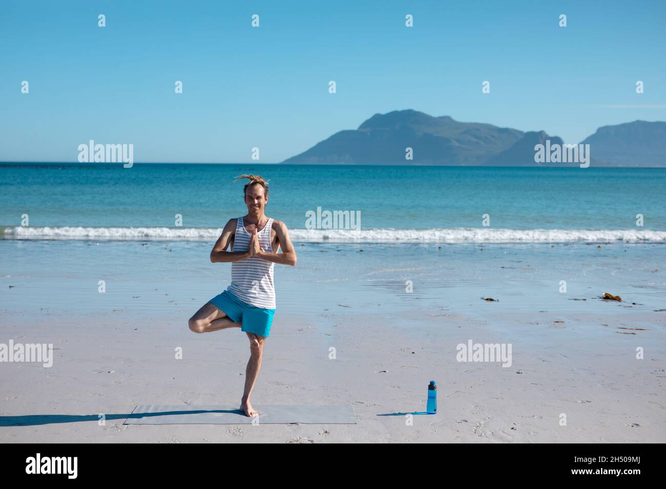 Mann, der Baum praktiziert, posiert Yoga-Haltung am Strand gegen klaren blauen Himmel mit Kopieplatz Stockfoto