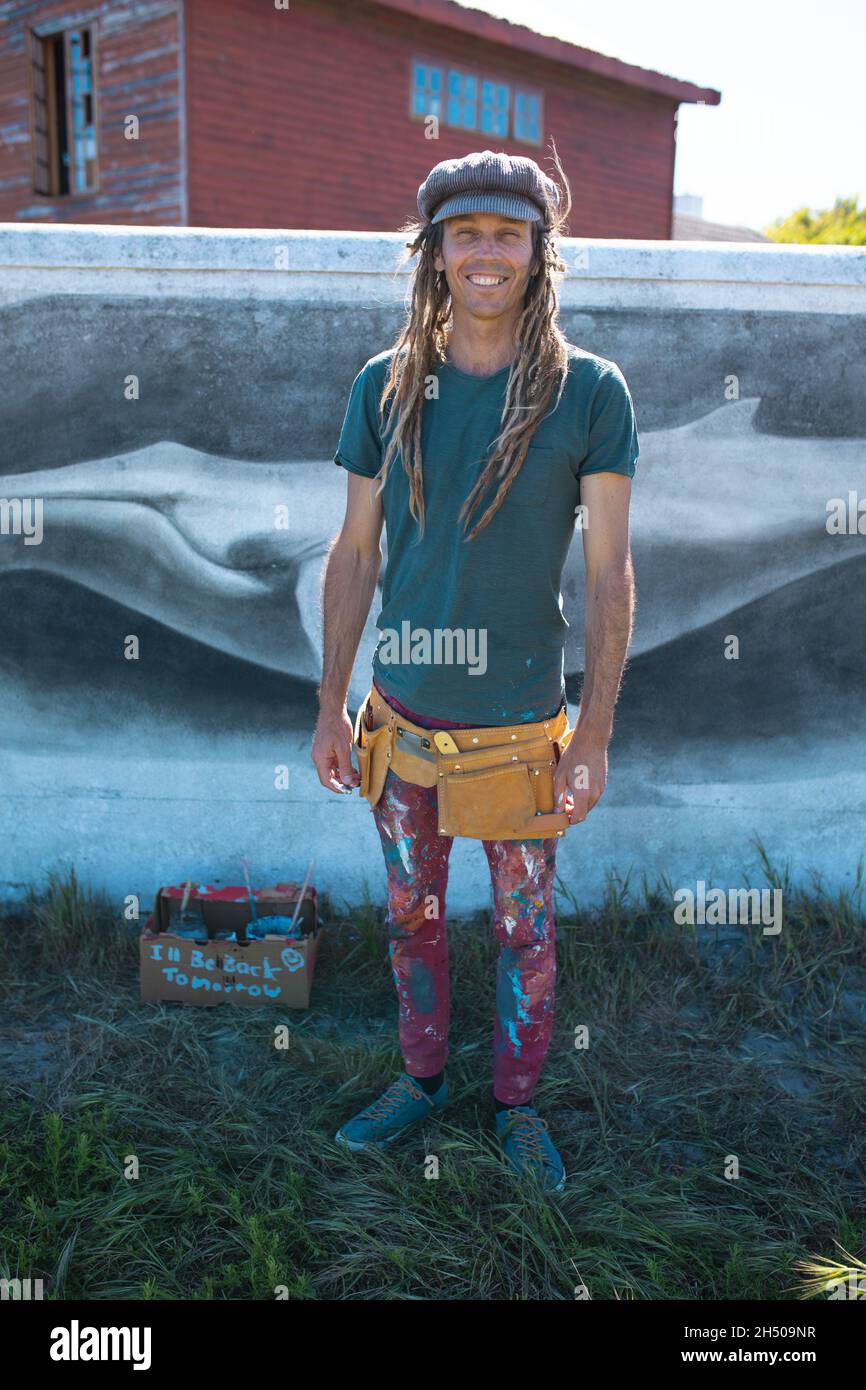 Lächelndes Porträt eines männlichen Hipster-Künstlers mit unordentlicher Kleidung, die gegen die Wandmalerei eines Wals steht Stockfoto