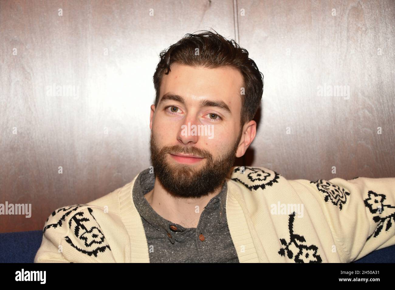 Der weißbärtige Mann sitzt abends in einem Restaurant mit unterschiedlichen Gesichtsausdrücken. Stockfoto