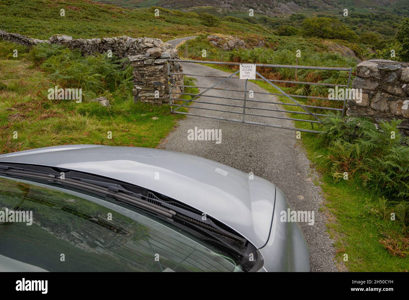 Das Auto wartet darauf, dass ein Tor auf einer eingezäunten Straße in den Hügeln von Nord-Wales in der Nähe von Harlech geöffnet wird. Stockfoto