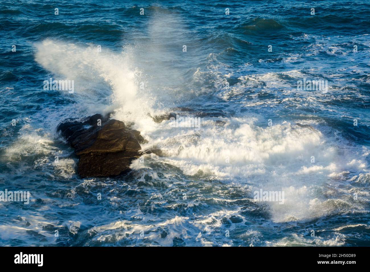 Wellen, die auf fast untergetauchte Felsen krachen und bei Flut eine potenzielle unsichtbare Gefahr darstellen Stockfoto