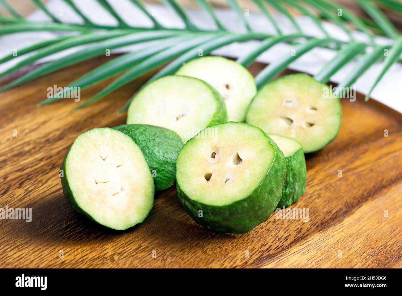 Frische grüne Feijoa (Ananas-Guava) Obstscheiben auf braunem Holzhintergrund in der Küche. Stockfoto