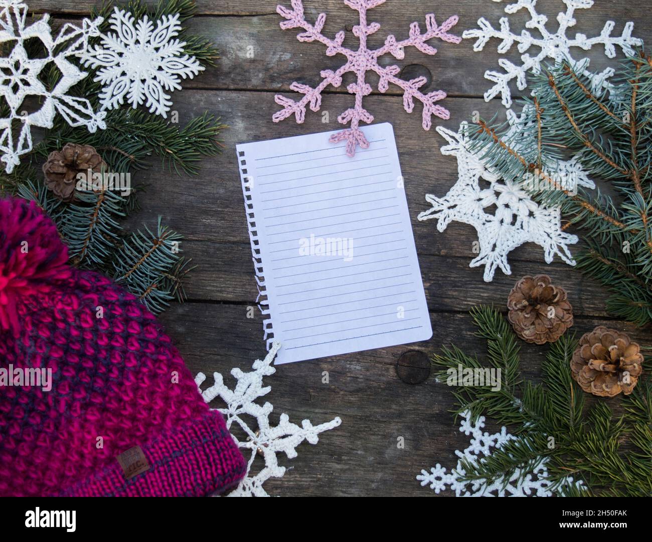 Häkeln Sie Schneeflocken-Ornamente auf Holzboden mit Platz für Text und Tannenzweig und Zapfen und einem gestrickten Bommel Hut Hintergrund Stockfoto