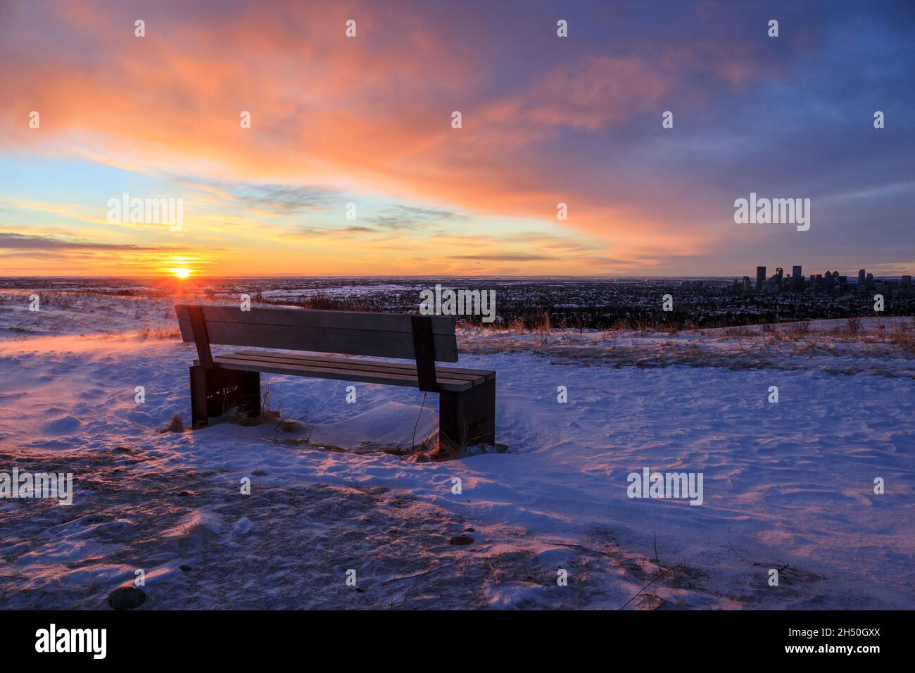 Leere Bank in einem Park mit Blick auf eine Stadt an einem verschneiten Morgen Stockfoto