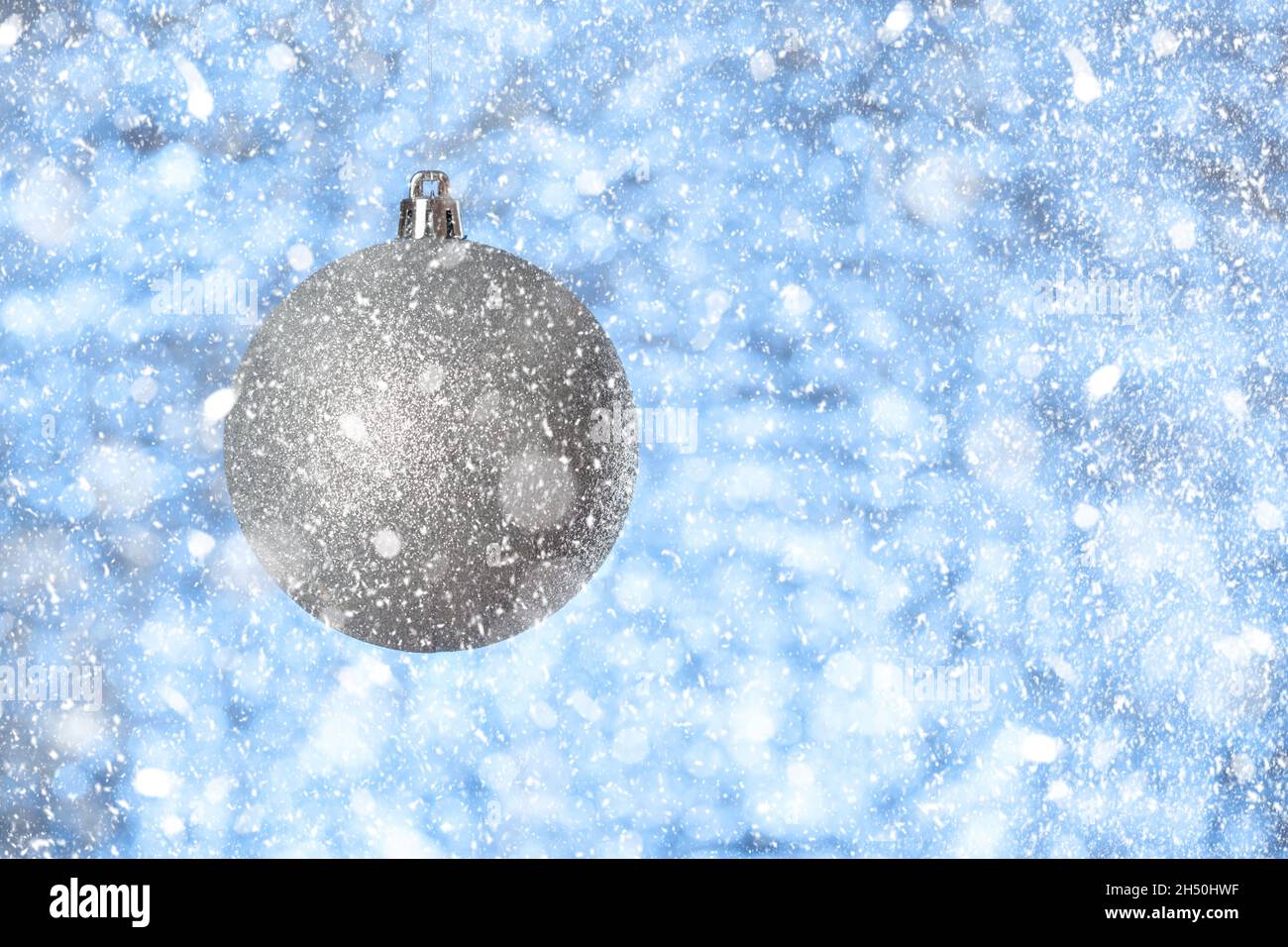 Silberner Weihnachtsball auf grau-blauem verschwommenem Hintergrund, Es schneit, Neujahrsgutschein, Kopierraum Stockfoto