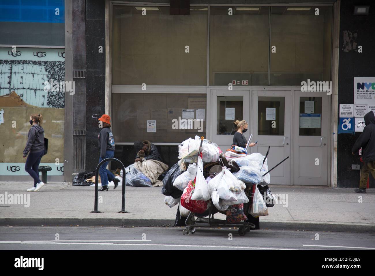 Die Habseligkeiten eines Obdachlosen parkten auf der 14th Street gegenüber dem Union Square, während er auf dem Bürgersteig unter Passanten in Manhattan, NYC, schläft. Stockfoto