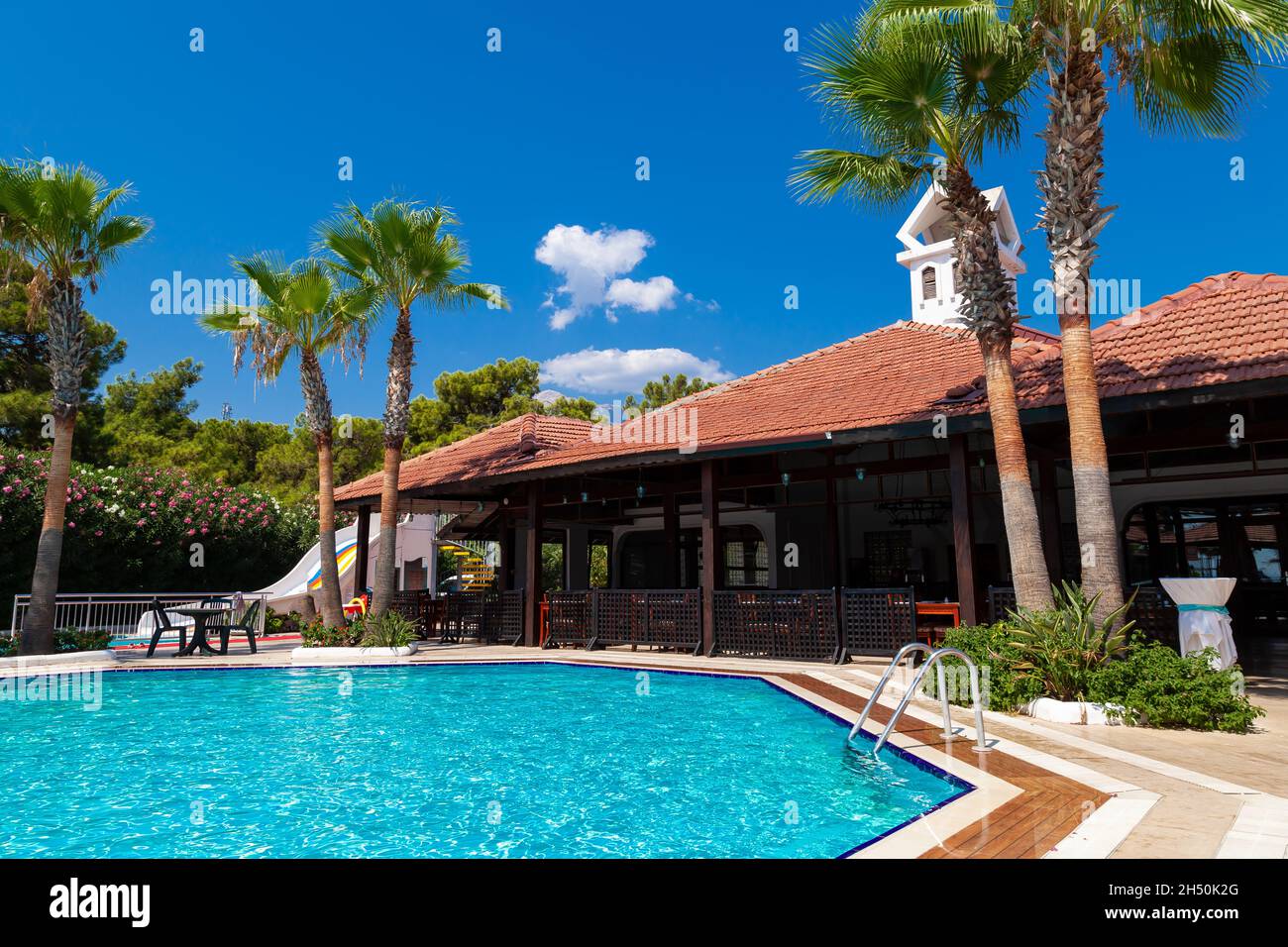 Hotel mit Swimmingpool, Palmen und Pinien. Touristen ruhen sich auf Sonnenliegen unter Sonnenschirmen aus. Reisen in die Pandemie. Stockfoto