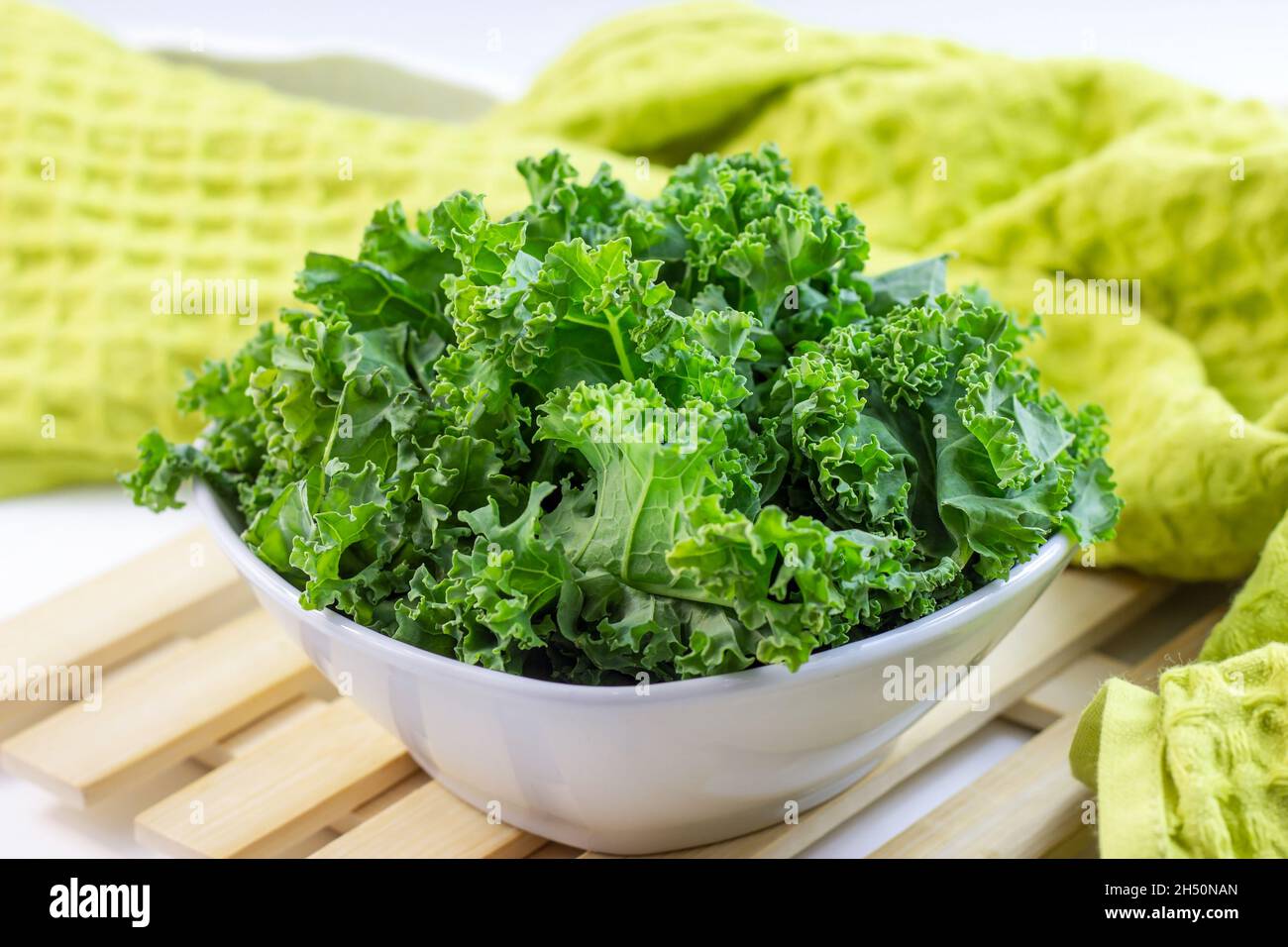 Frisches grünes Lockenkohl oder Grünkohl-Salatblätter, die auf hellem Hintergrund auf dem Tisch in der Küche in die Schüssel geschnitten werden. Stockfoto
