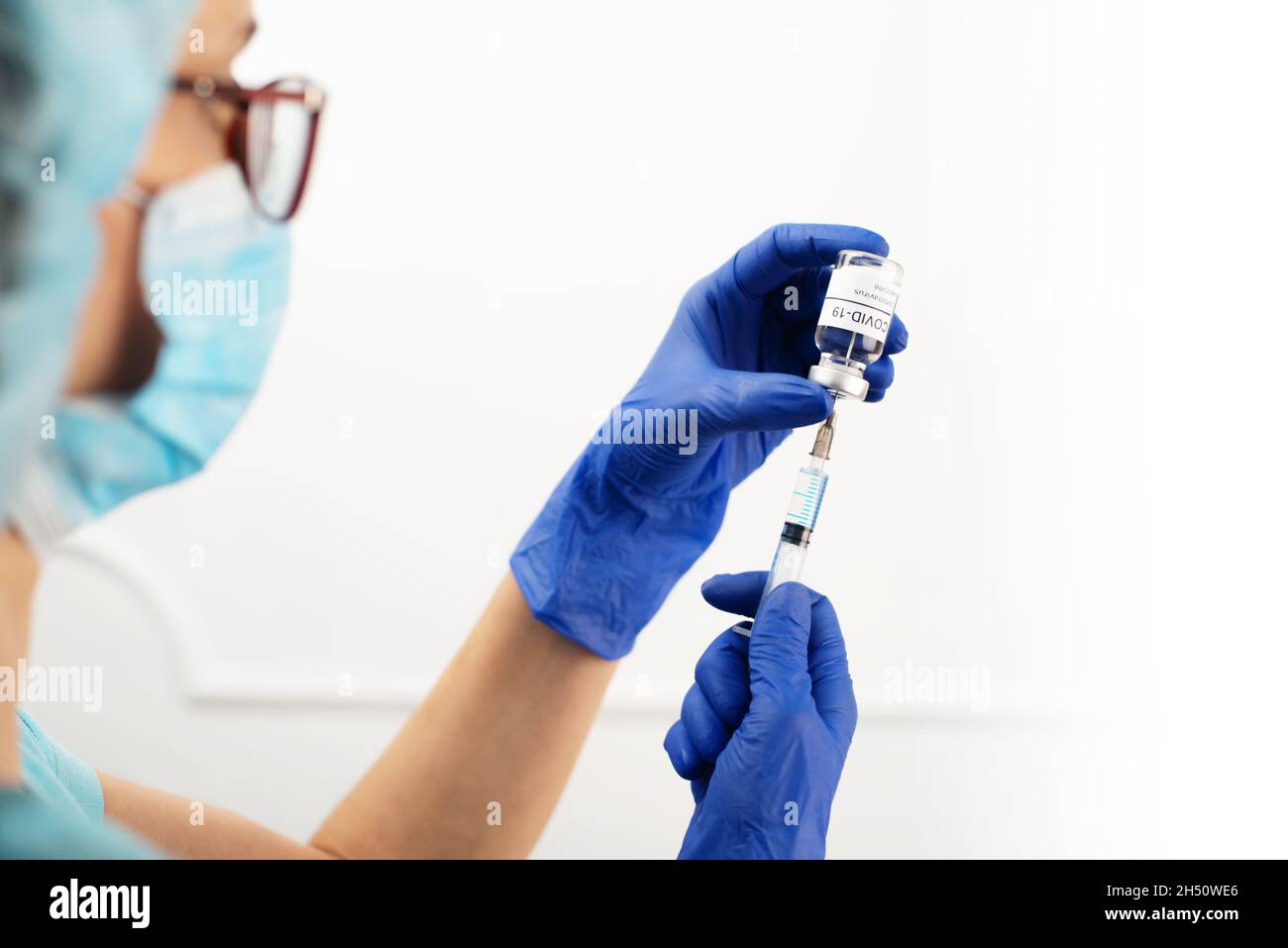 Kaukasische Ärztin mittleren Alters mit Schutzbrille und Handschuhen, die eine Spritze für die Injektion des Coronavirus-Impfstoffs vorbereitet Stockfoto