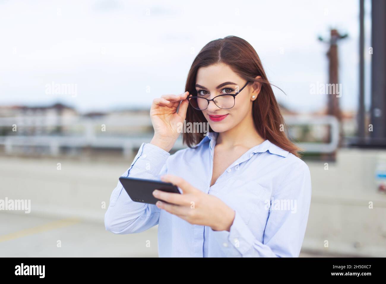 Junge Nerd Rotschopf kaukasischen Geschäftsfrau hält Smartphone im Freien Stockfoto