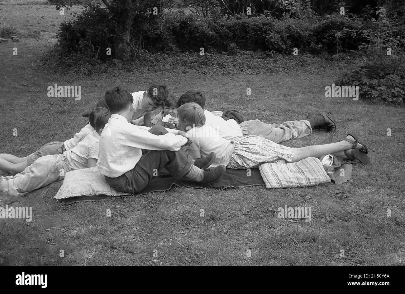 1950, historisch, eine Gruppe von kleinen Kindern, die auf Decken und Kissen auf dem Gras zusammen liegen und möglicherweise ein Kartenspiel spielen, England, Großbritannien. Stockfoto