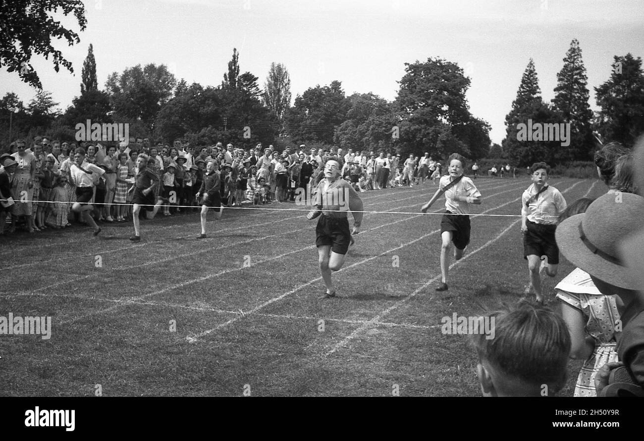 1950s, historisch, Schulsport, Zuschauer, die Schüler beobachten, die bei einem Sprint-Rennen auf einem Grassportfeld antreten, wobei das Abschlussband für die jungen Athleten in Sicht ist, England, Großbritannien. Stockfoto