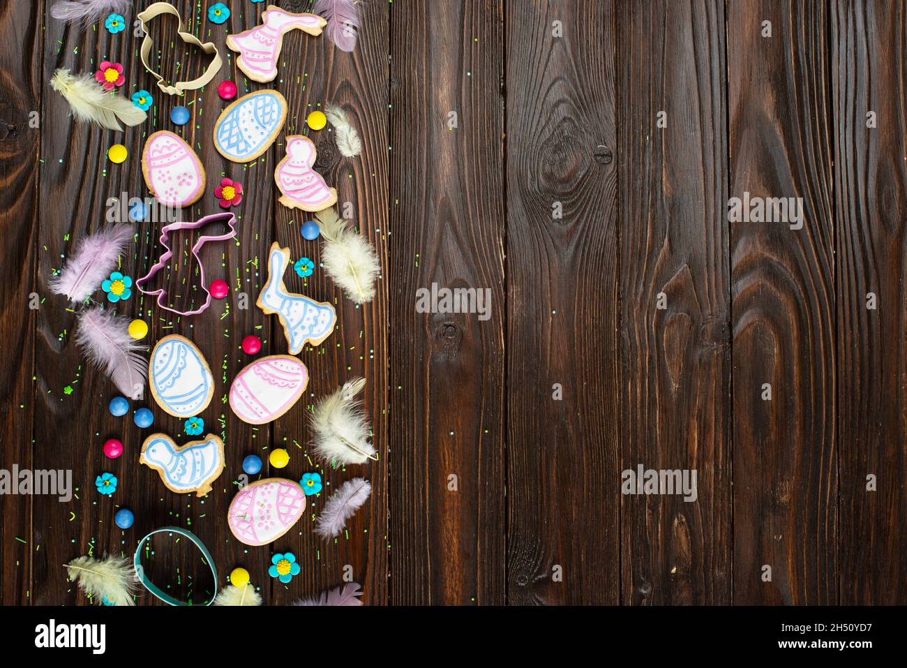 Zuckerstreuseln, Süßigkeiten, Federn, Ausstechformen, Ostergrüßkekse in Form von Hühnchen und Kaninchen auf Holztisch-Hintergrund. Flach Lay moc Stockfoto