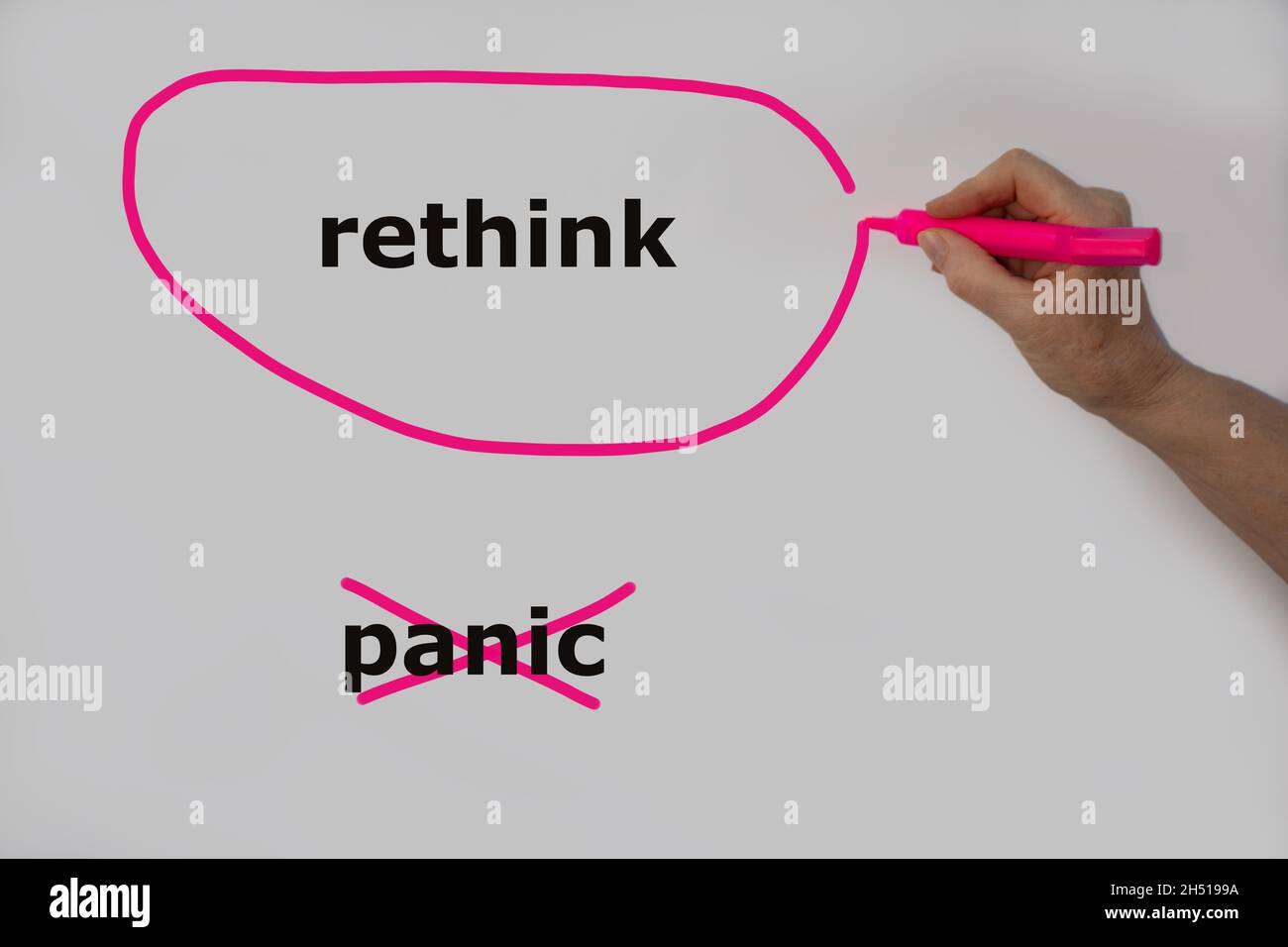 Rethink als Alternative zur Panik wird mit einer Hand auf eine weiße Wand geschrieben, rethink ist mit einem pinken Stift umrandet und Panik wurde durchgestrichen Stockfoto