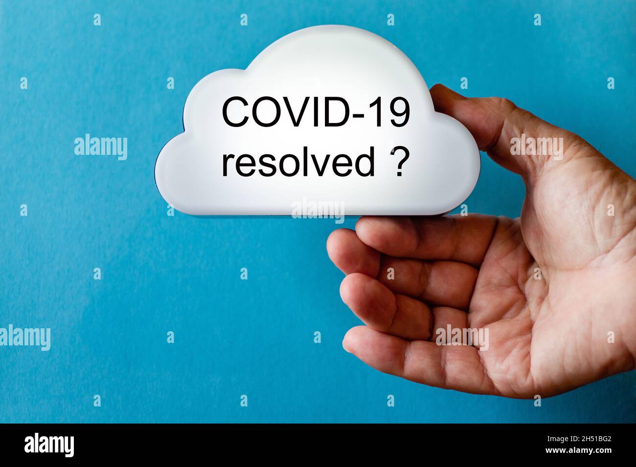 Die Hand hält ein weißes Wolkensymbol vor einem blauen Hintergrund. Der Text wird auf die Wolke geschrieben: COVID-19 aufgelöst ? Stockfoto
