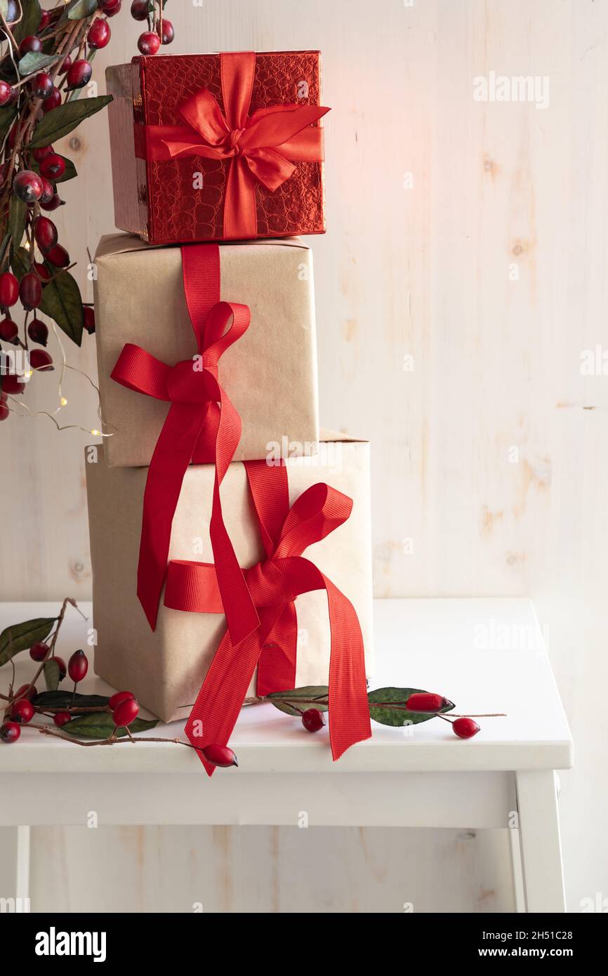 Drei Weihnachtsgeschenke in einem Turm auf weißem Hintergrund mit einem Rand aus roten Beeren und weihnachtsbeleuchtung mit Kopierraum gestapelt Stockfoto