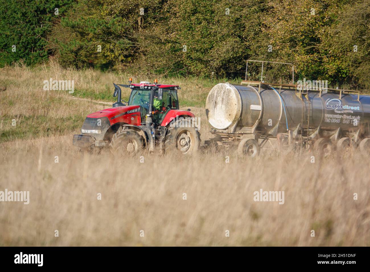 Ein großer Red Case 340 Magnum Traktor schleckt einen 30 Tonnen schweren Wasseranhänger über Ackerland Stockfoto