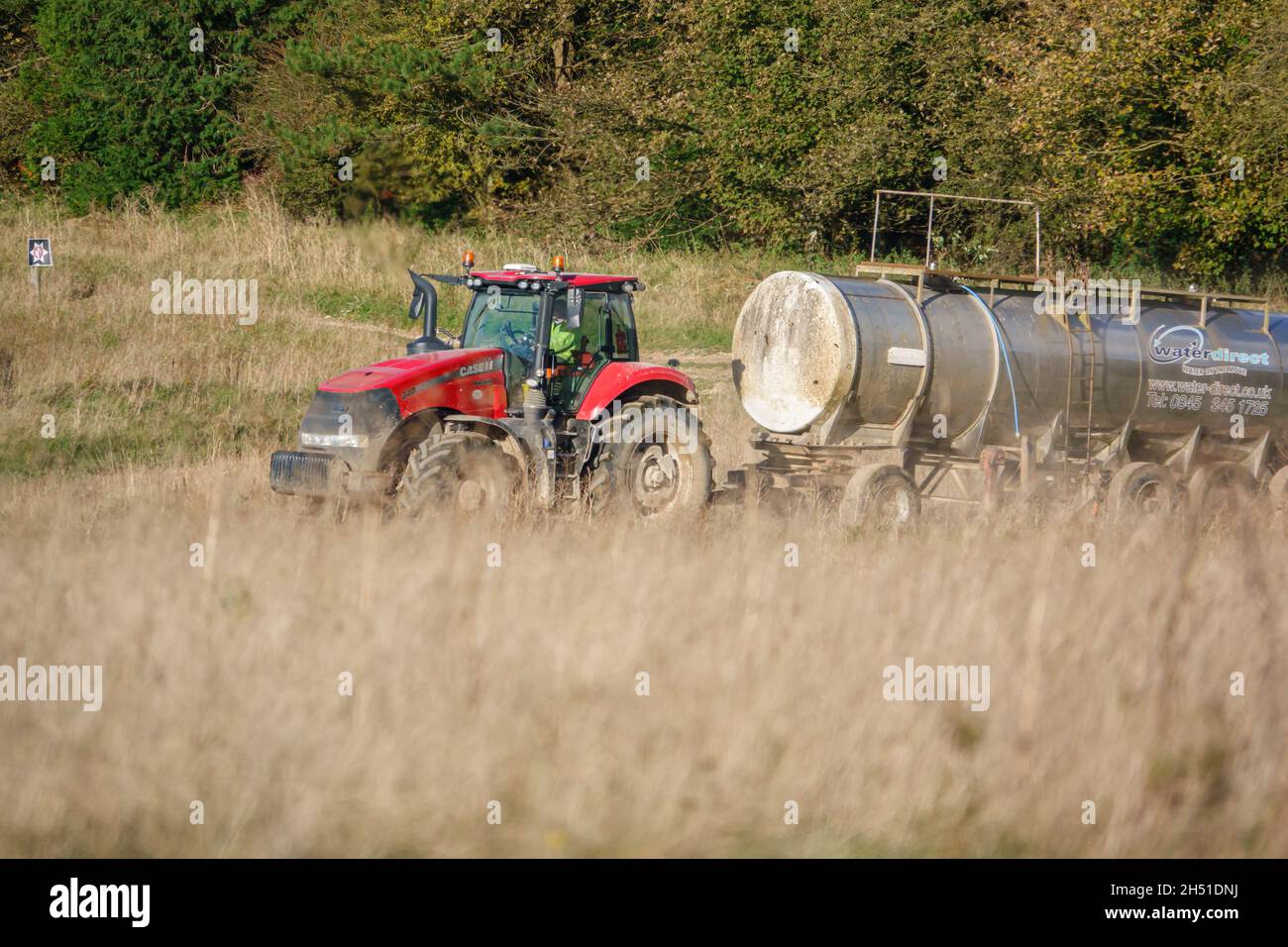 Ein großer Red Case 340 Magnum Traktor schleckt einen 30 Tonnen schweren Wasseranhänger über Ackerland Stockfoto