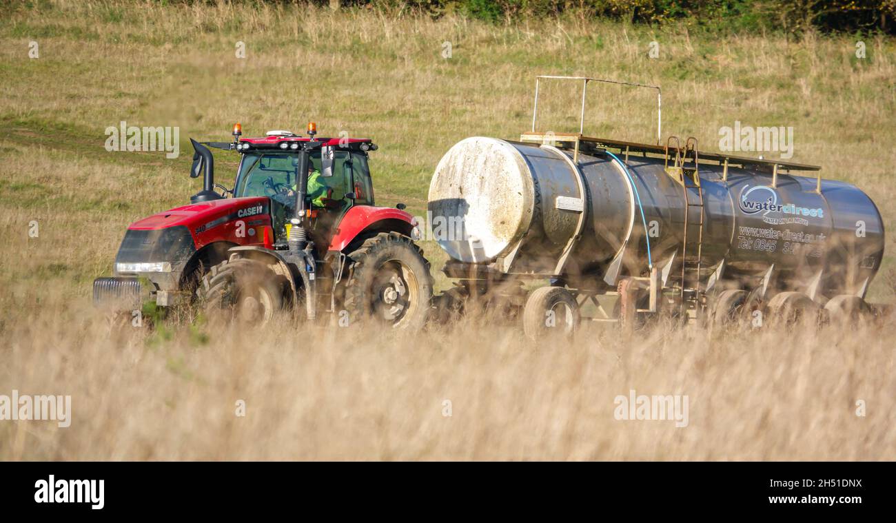 Ein großer Red Case 340 Magnum Traktor schleckt einen 30 Tonnen schweren Wasseranhänger über Ackerland Stockfoto