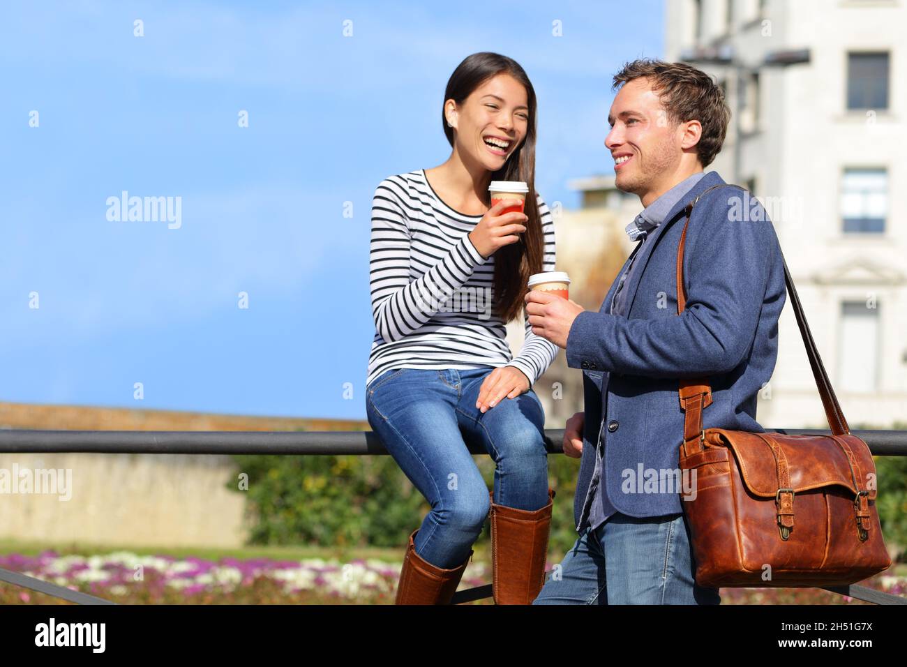 Freunde unterhalten sich beim Kaffeetrinken in der Mittagspause in der Frühlingssonne auf der Stadtstraße. Glückliche multirassische paar Arbeiter genießen Café Date zusammen Stockfoto