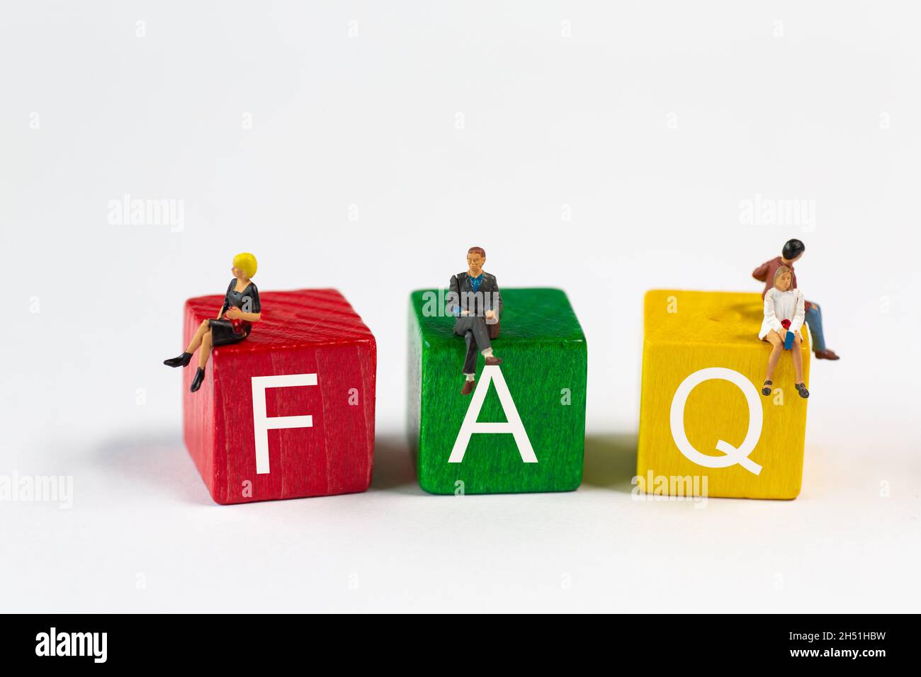FAQ - die Abkürzung für Frequently Asked Questions ist in weißer Schrift auf roten, grünen und gelben Bausteinen. Kleine Plastikfiguren sitzen auf den Blöcken Stockfoto