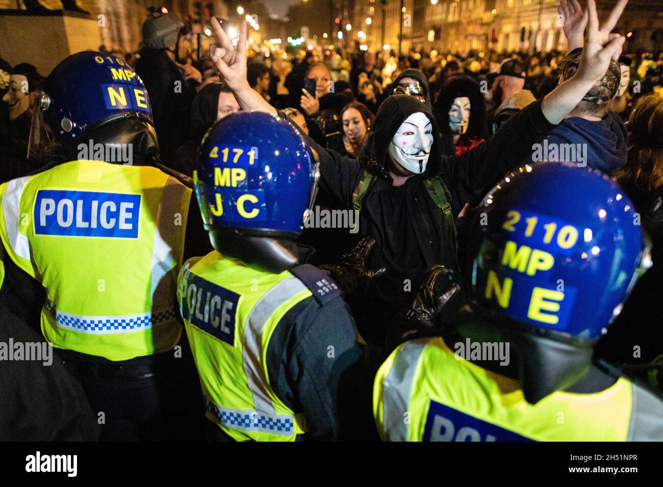 London, Großbritannien. November 2021. Eine Person, die mit einer anonymen Maske bekleidet ist, wird vor dem Parlamentsgebäude von der Polizei für den jährlichen Millionen-Maske-marsch durch die Stadt umgeben. Die Anonymous-Bewegung steht solidarisch für eine Gesellschaft, die von der politischen Elite und den assoziierten Unternehmen marginalisiert wird. Kredit: Andy Barton/Alamy Live Nachrichten Stockfoto