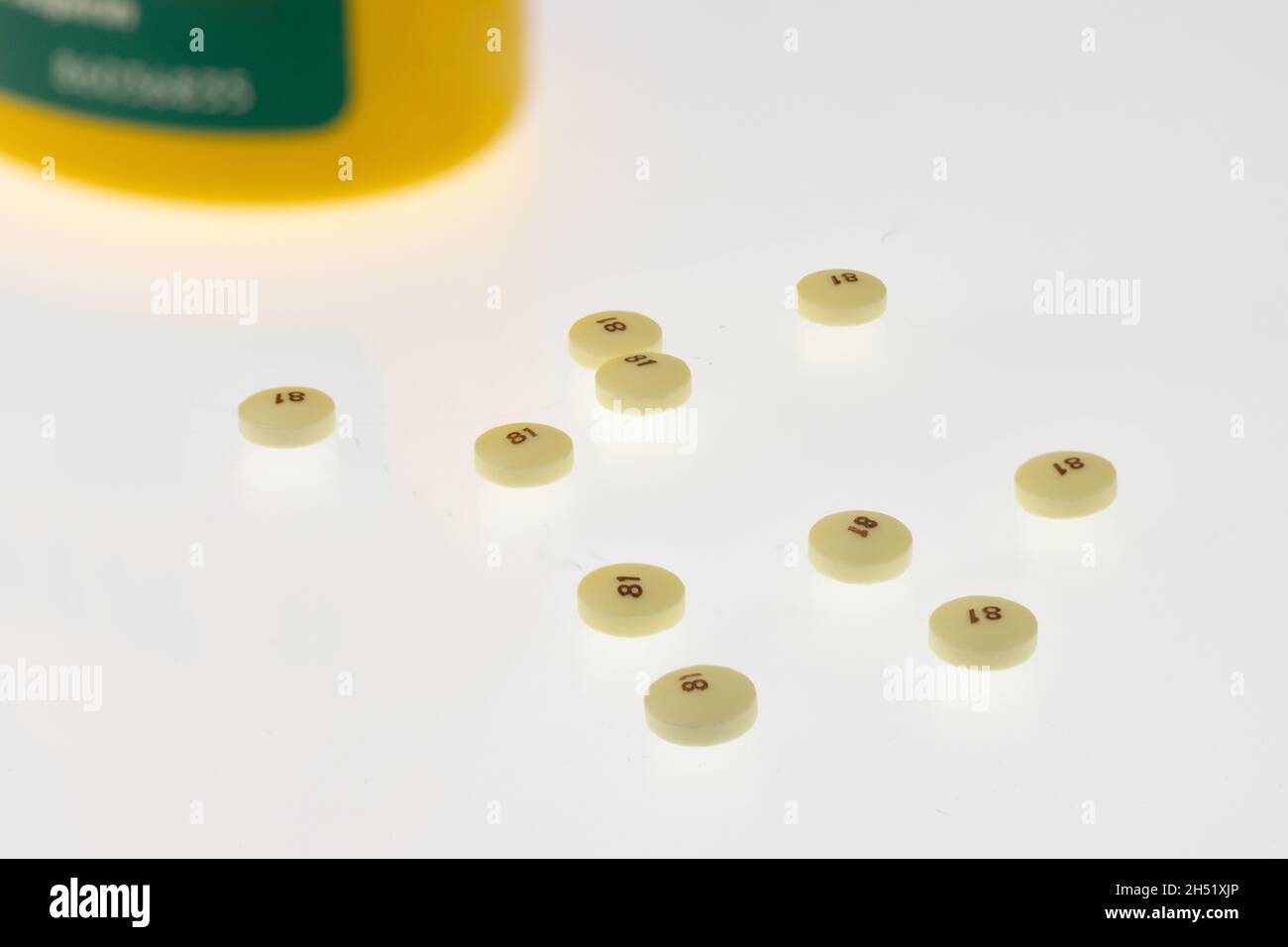 Gestreute niedrige Dosis 81 Milligramm Aspirin auf weißem Hintergrund mit einer gelben und grünen Flasche im Hintergrund, häufig als Präventivmedizin für verwendet Stockfoto