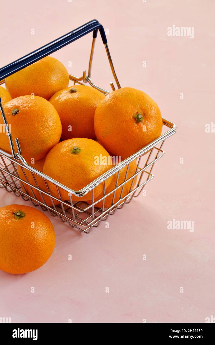Leuchtend orange Mandarinenorangen im Mini-Warenkorb auf hellrosa Hintergrund. Vertikales Format mit Platz für Text. Stockfoto