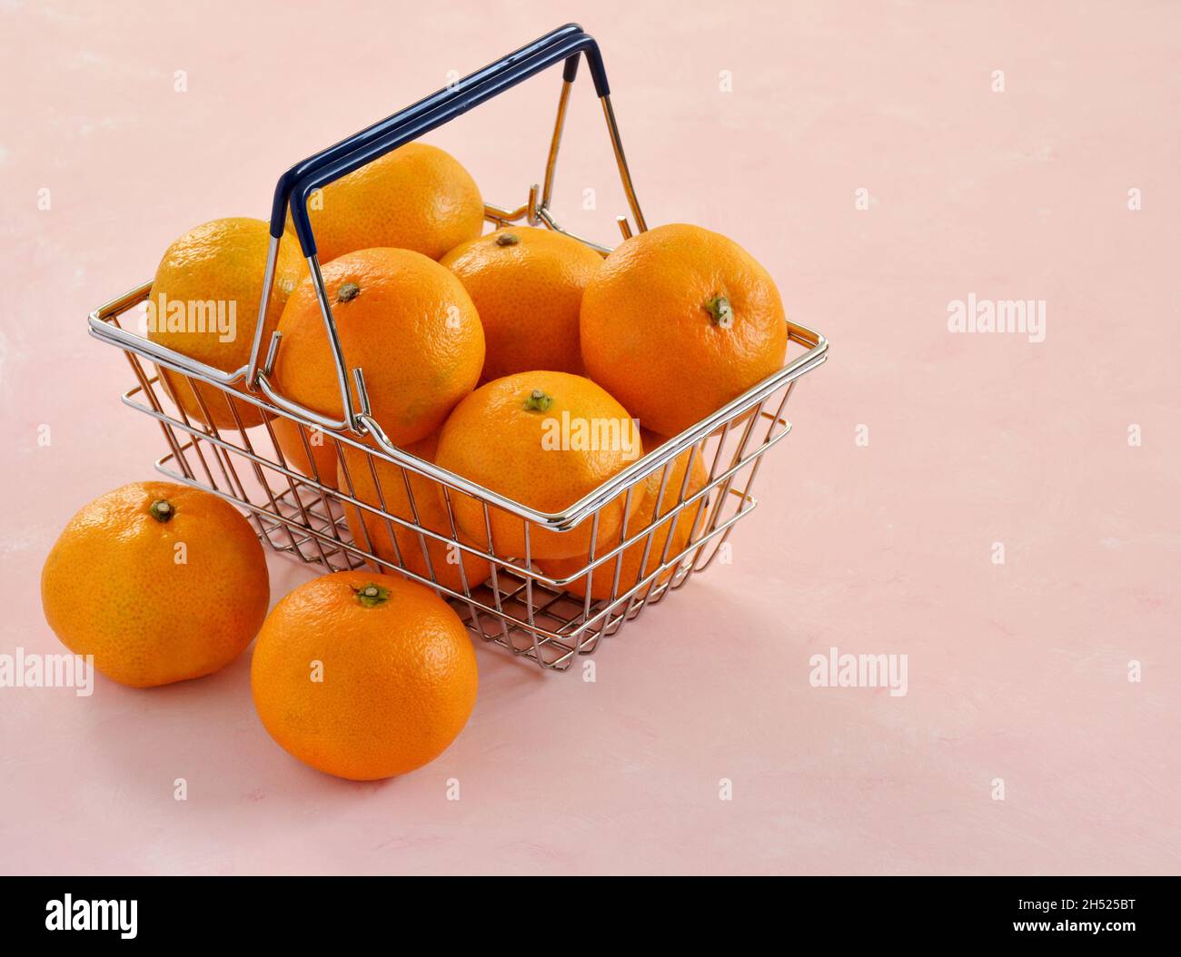 Leuchtend orange Mandarinenorangen im Mini-Warenkorb auf hellrosa Hintergrund. Horizontales Format mit Platz für Text. Stockfoto