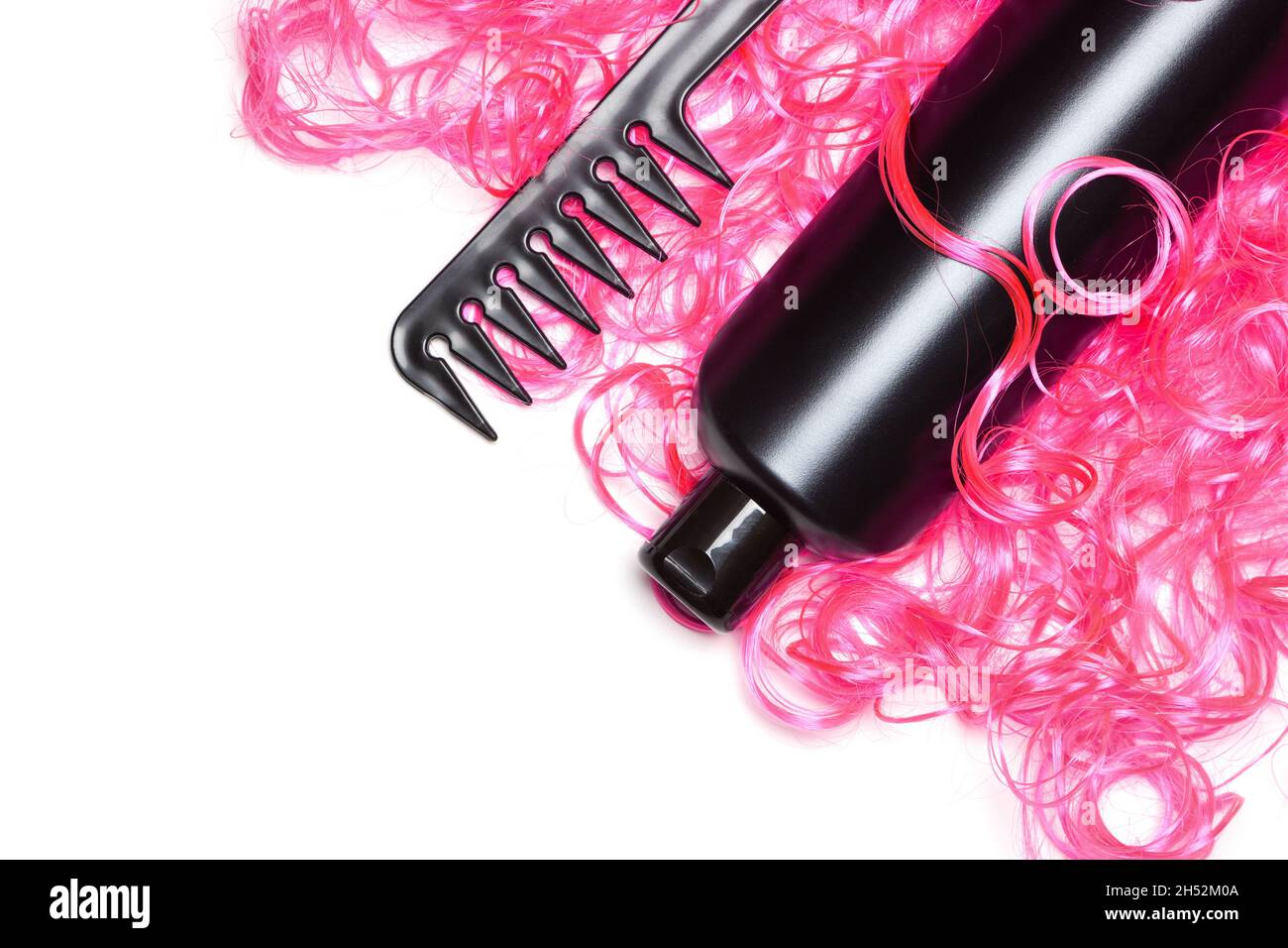 Nahaufnahme der Kosmetikflasche mit breitem Zahnkamm und leuchtend rosa Puppenhaar auf Weiß. Lockiges Haarpflege- und Styling-Produkte Konzept, Kopierraum Stockfoto