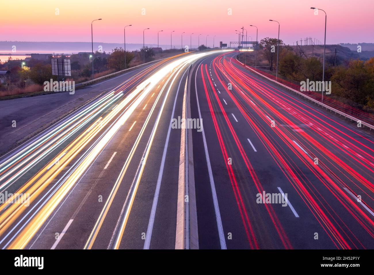 Vorstadtautobahn am Abend nach Sonnenuntergang. Spuren von Scheinwerfern und Schlussleuchten bei starkem Verkehr Stockfoto