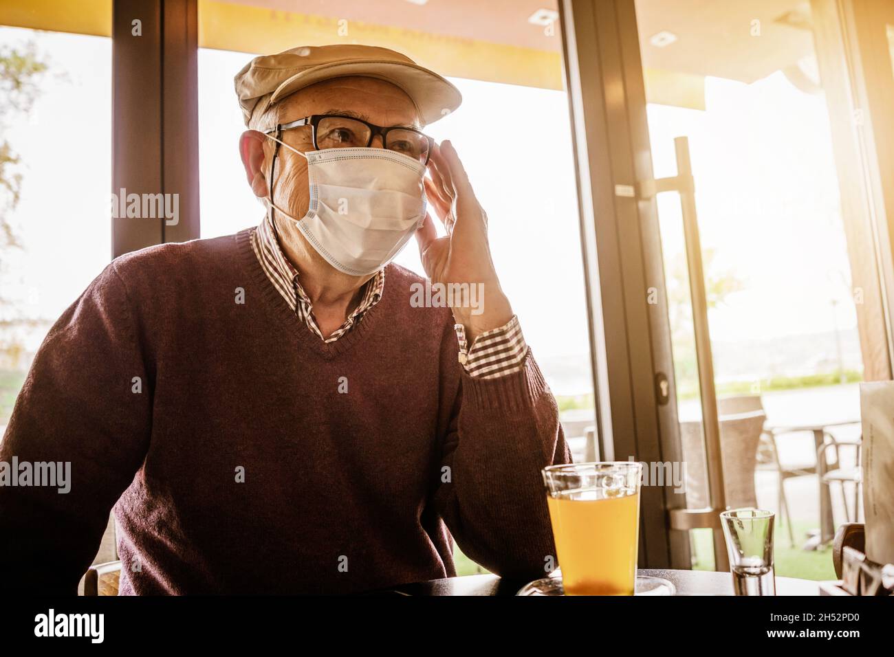 Älterer Mann sitzt im Café mit Gesichtsschutzmaske. Covid 19 Präventionskonzept. Stockfoto
