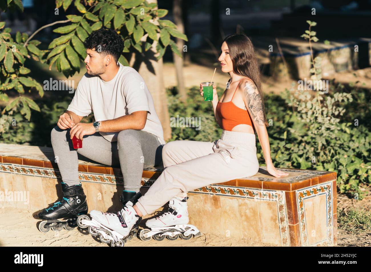 Zwei junge Freunde trinken alkoholfreie Getränke, während sie in Inline-Skates sitzen Stockfoto