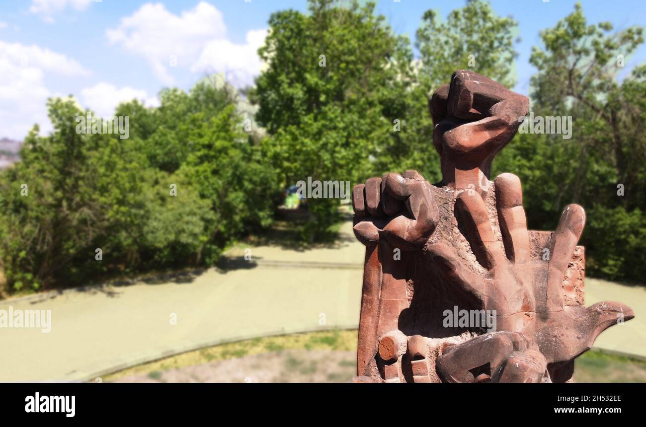 Tuffstein erhöhte Hände Denkmal Statue für diejenigen, die leiden Kampf nie aufgeben und kämpfen, in einem Park mit blauem Himmel und grünen Bäumen auf der Rückseite Stockfoto