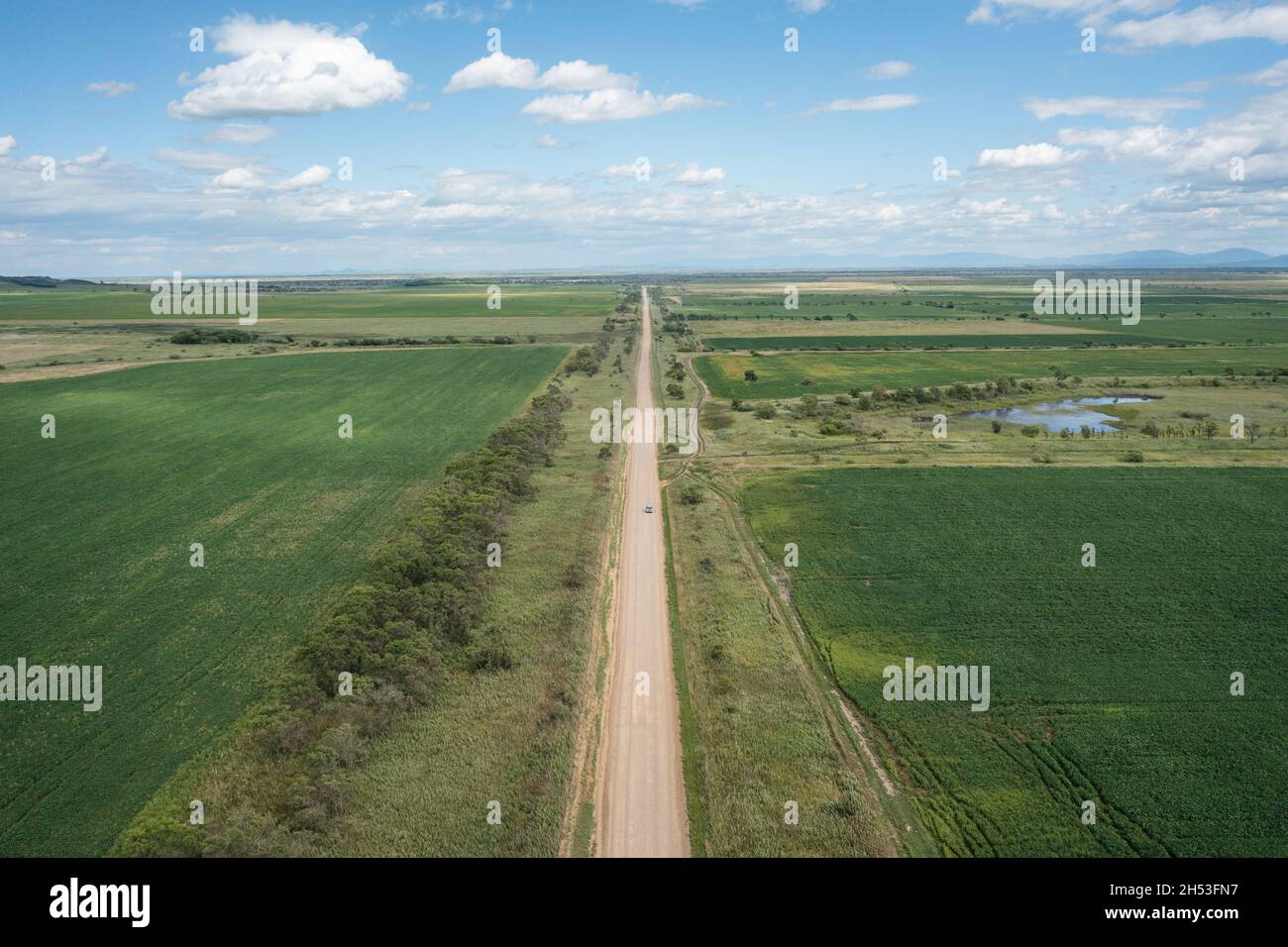Eine Landstraße zwischen den Feldern, die sich bis in die Ferne erstreckt, fährt ein Auto entlang. Stockfoto