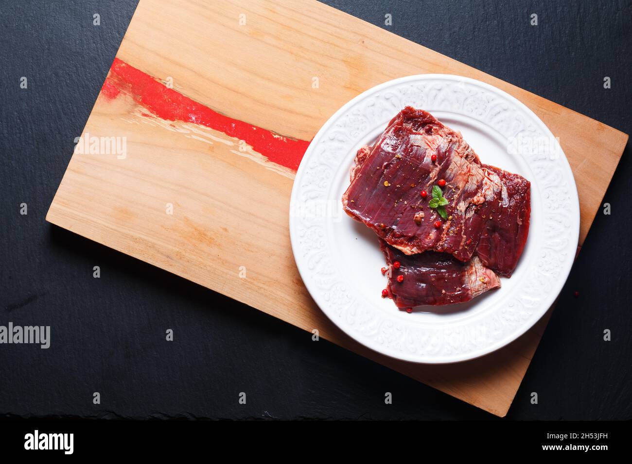 Food Concept Fresh RAW Rock Steak in weißer flacher Keramikplatte auf Holzbrett und schwarzer Schiefersteinplatte mit Kopierfläche Stockfoto