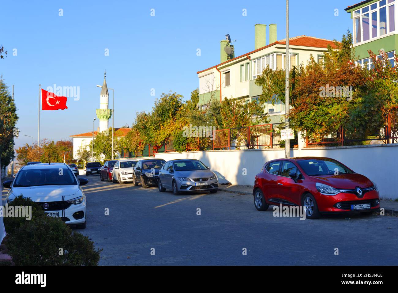 Autos, die an einer normalen Straße in der Türkei mit türkischer Flagge und Minarett geparkt sind Stockfoto