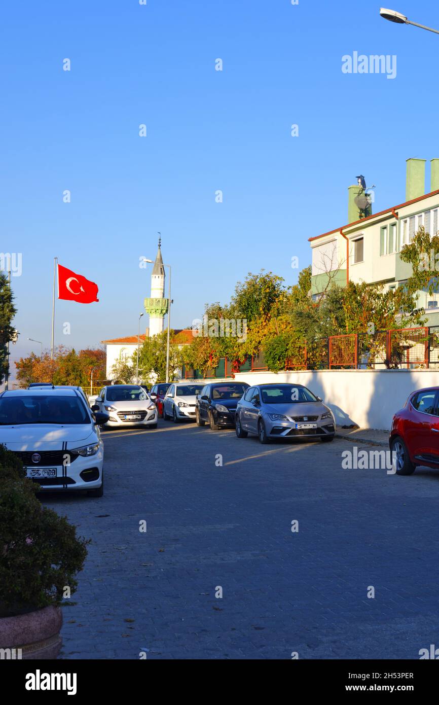 Autos, die an einer normalen Straße in der Türkei mit türkischer Flagge und Minarett geparkt sind Stockfoto