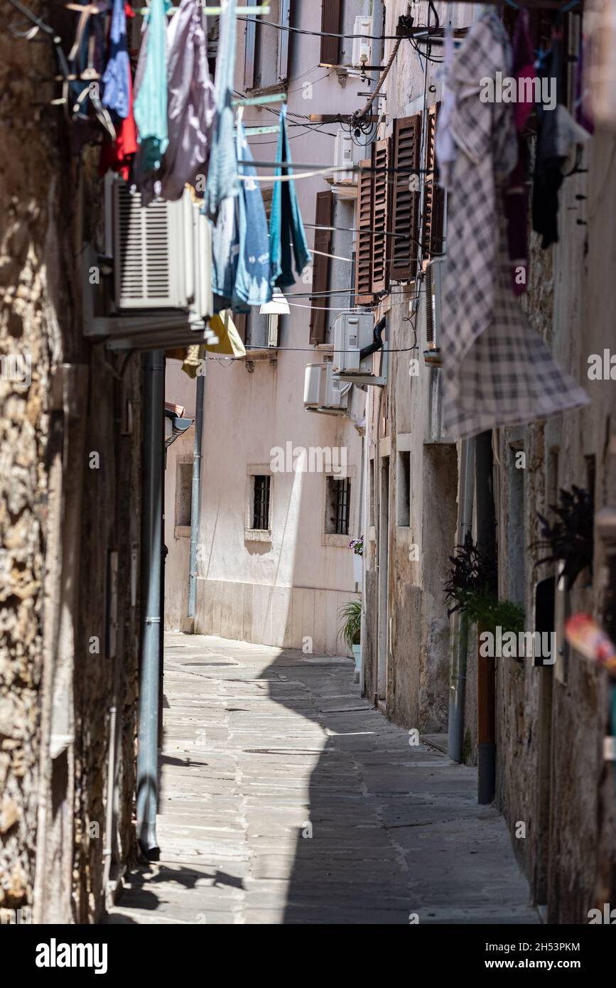 Koper, Slowenien - 12. Juli 2021: Enge Straße zwischen alten, baufälligen Stadthäusern. Kleidung hing zwischen Gebäuden. Stockfoto