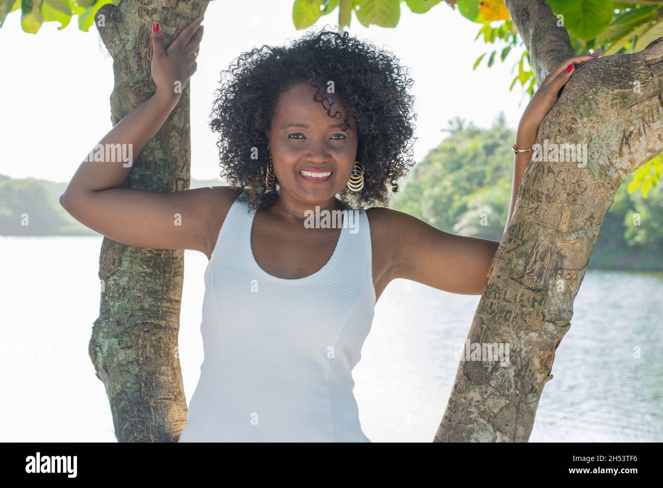 Bela modelo em um vestdo branco sorrindo e olhando para a câmera. AO Fundo, árvores, plantas, flores e o rio na paisagem. Salvador, Bahia, Brasilien. Stockfoto