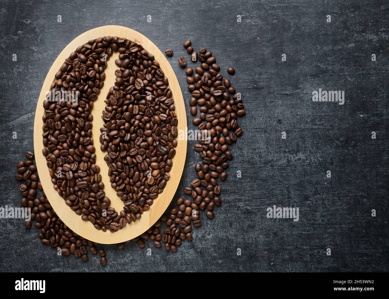 Frisch geröstete Kaffeebohnen auf einem Holzteller, grauer Grunge-Hintergrund mit Platz für Text Stockfoto