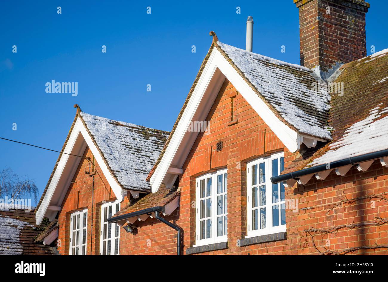 Altes Haus mit schlichten Lehmdachziegeln, Schnee auf dem Dachdach im Winter, Großbritannien. Dachisolierung und Konzepte zur Verbesserung der Wohnqualität. Stockfoto