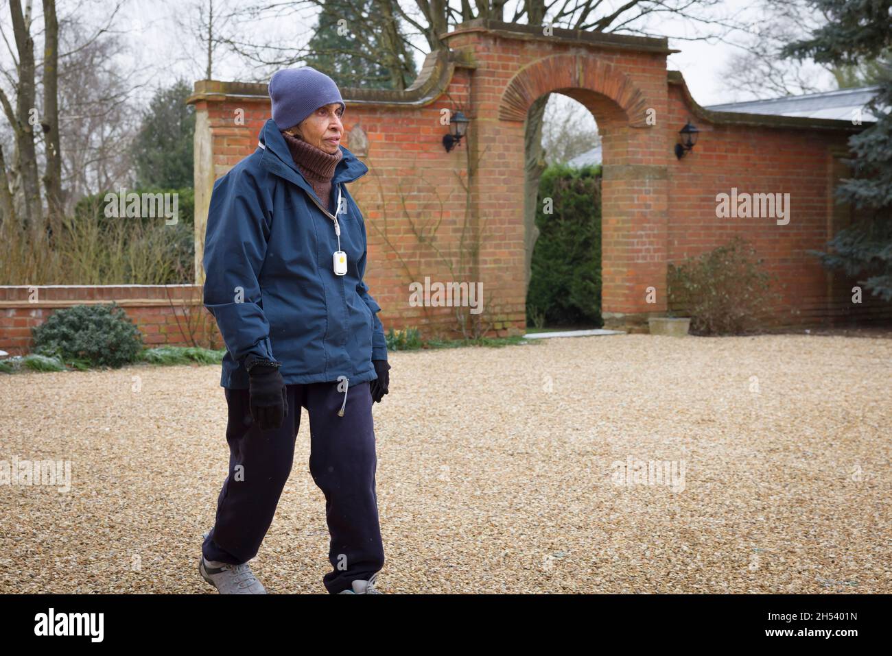 Ältere asiatische indische Frau, die im Winter im Freien geht, Sport macht, Großbritannien. Tragen Sie warme Kleidung und einen SOS-Anhänger mit persönlichem Sicherheitsalarm Stockfoto