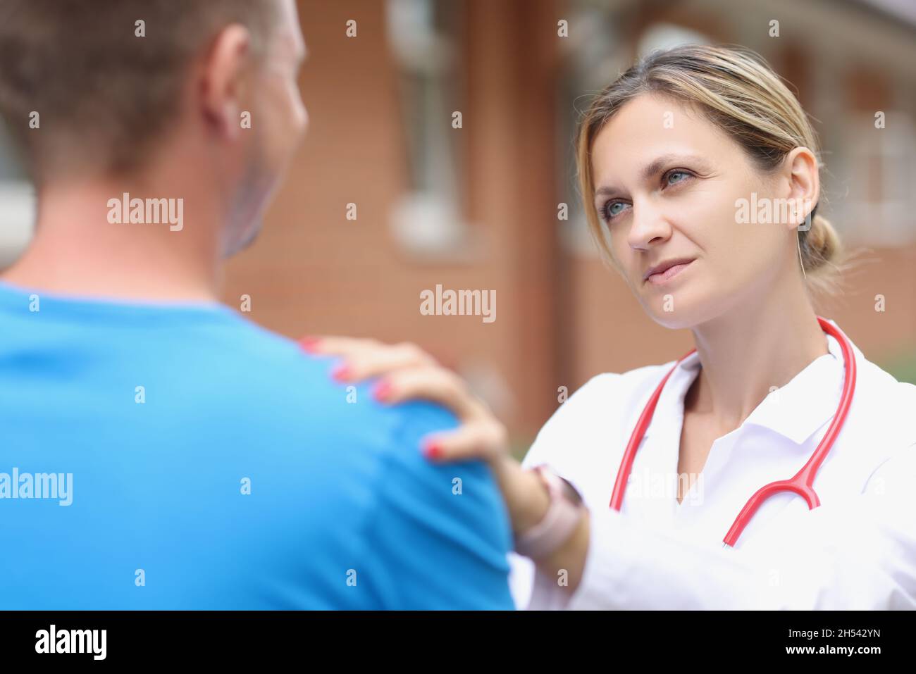 Ärztin legt die Hand auf die Schulter des Patienten, um sich zu beruhigen Stockfoto