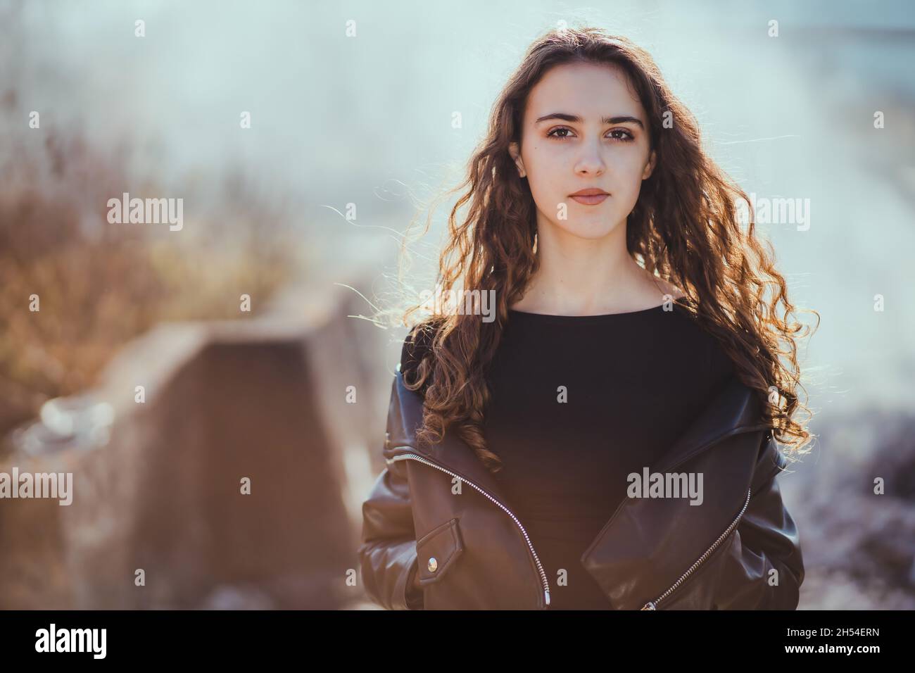 Outdoor-Porträt eines schönen Teenager Brünette Mädchen in der schwarzen Lederjacke mit Rauch im Hintergrund Stockfoto