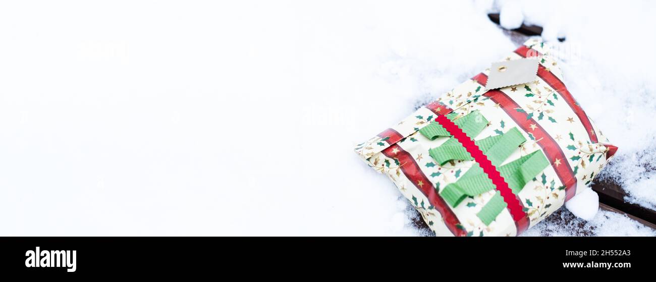 Weihnachtsgeschenk im Schnee. Horizontales Banner, leerer Kopierbereich. Wunderschön eingewickelt präsentieren im Freien in natürlicher Umgebung während der Winterferien liegen. Stockfoto