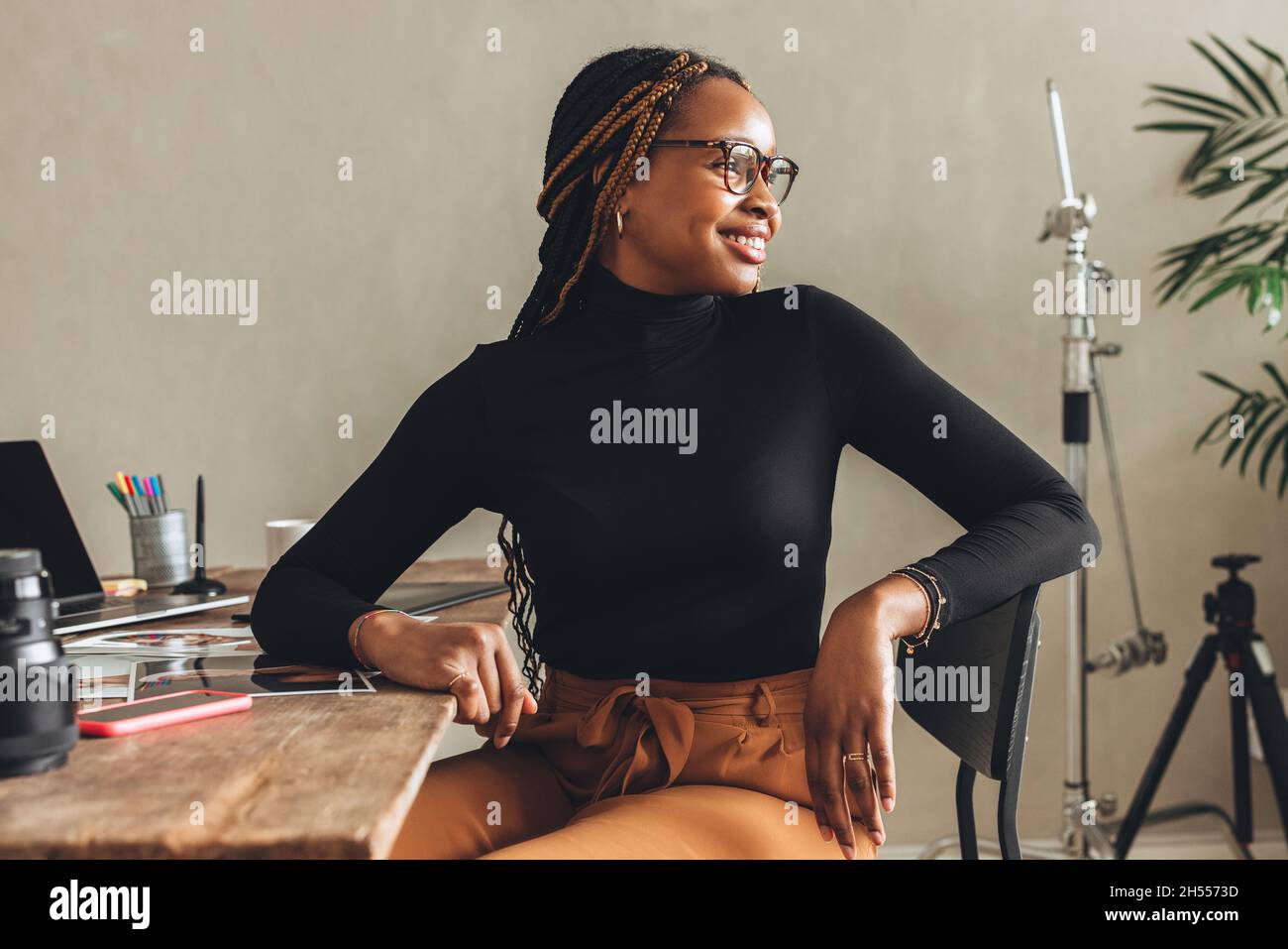 Denken an neue kreative Ideen. Fröhliche junge Fotografin lächelt, während sie nachdenklich davonschaut. Kreative Freiberuflerin, die an einem neuen p Stockfoto