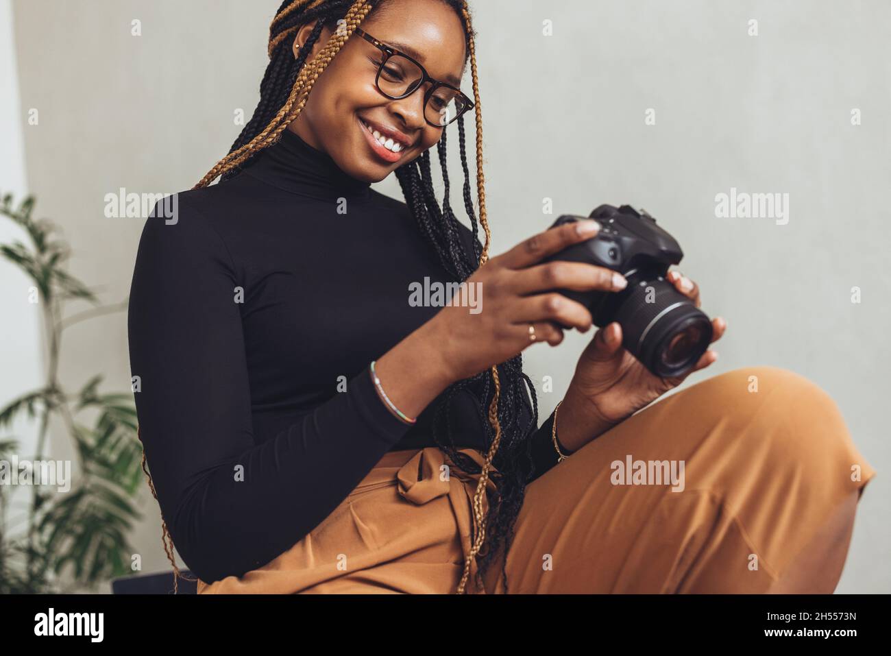 Machen Sie einige Kameraarbeiten. Fröhliche Fotografin, die fröhlich lächelt, während sie eine dslr-Kamera in ihrem Heimbüro hält. Künstlerische junge freiberufliche arbeiterei Stockfoto